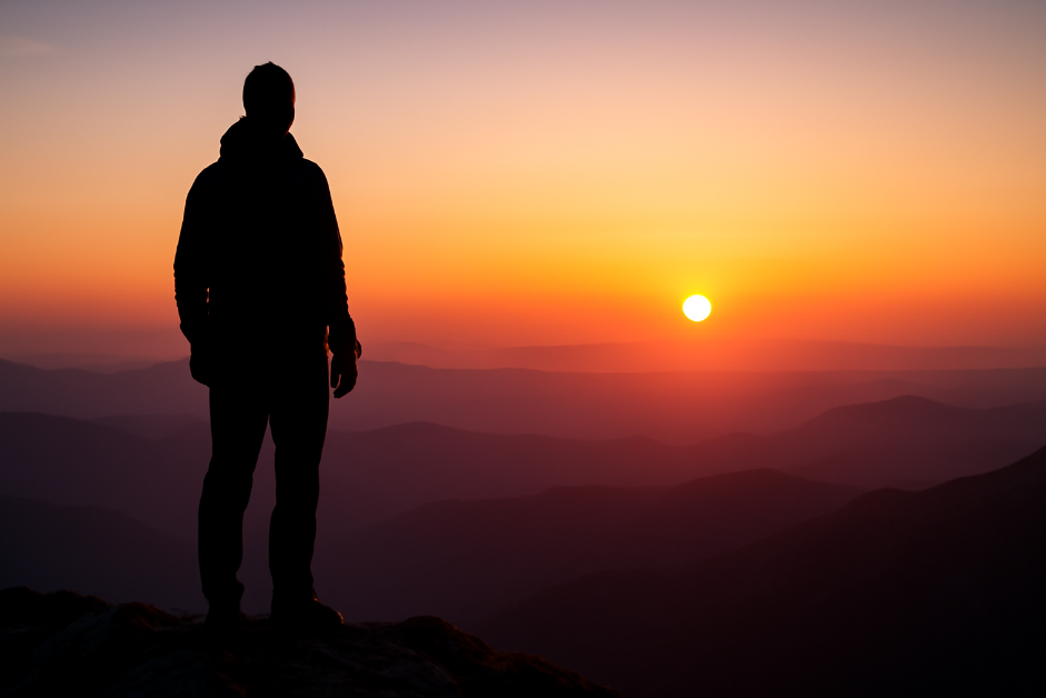 Silhouette of a person standing on a mountain peak during sunset, symbolizing long-term strategic thinking, patience, and vision for future success.
