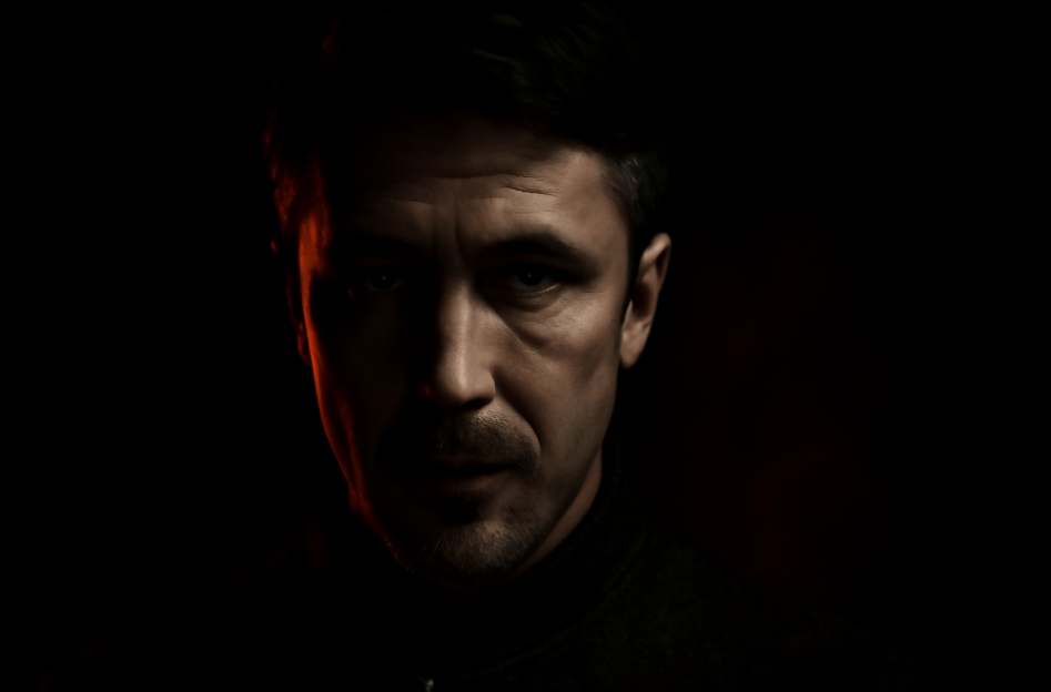 Close-up of Littlefinger from Game of Thrones with half of his face in shadow, a calculating expression, and his eyes illuminated, symbolizing strategy and manipulation, with a subtle red glow to suggest power.