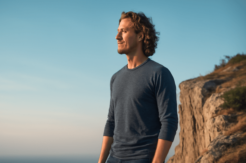 A confident young man standing at the edge of a cliff, gazing ahead with a serene and hopeful expression, symbolizing clarity, purpose, and self-reflection against a calm sky.